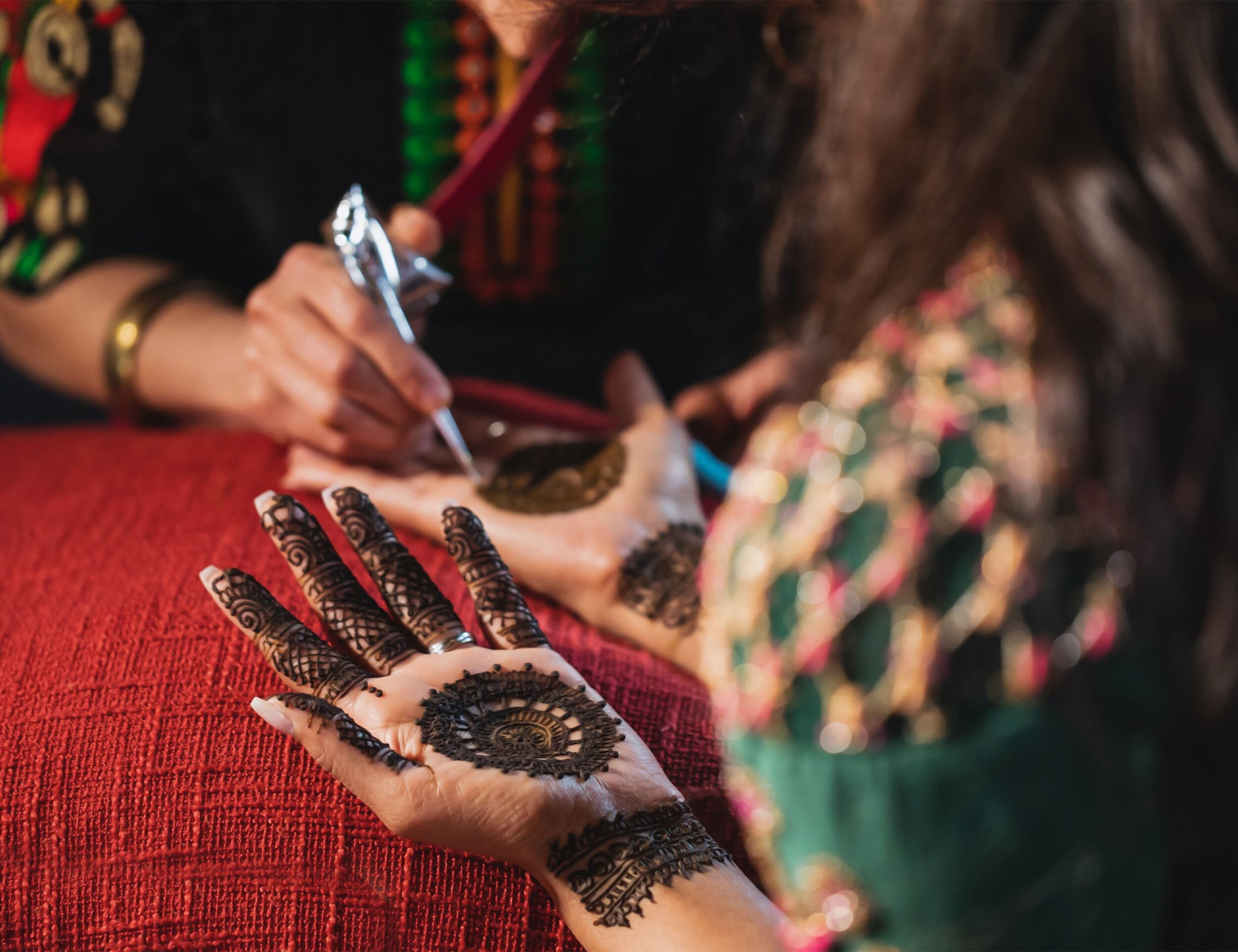 Bride having her hands adorned with bridal mehendi by a professional mehendi artist.